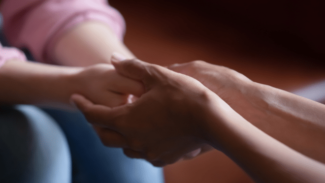 Close up of hands of a caregiver holding hands of a woman.