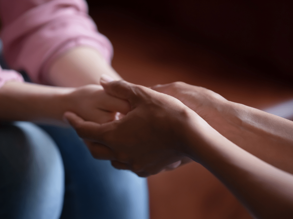 Close up of hands of a caregiver holding hands of a woman.