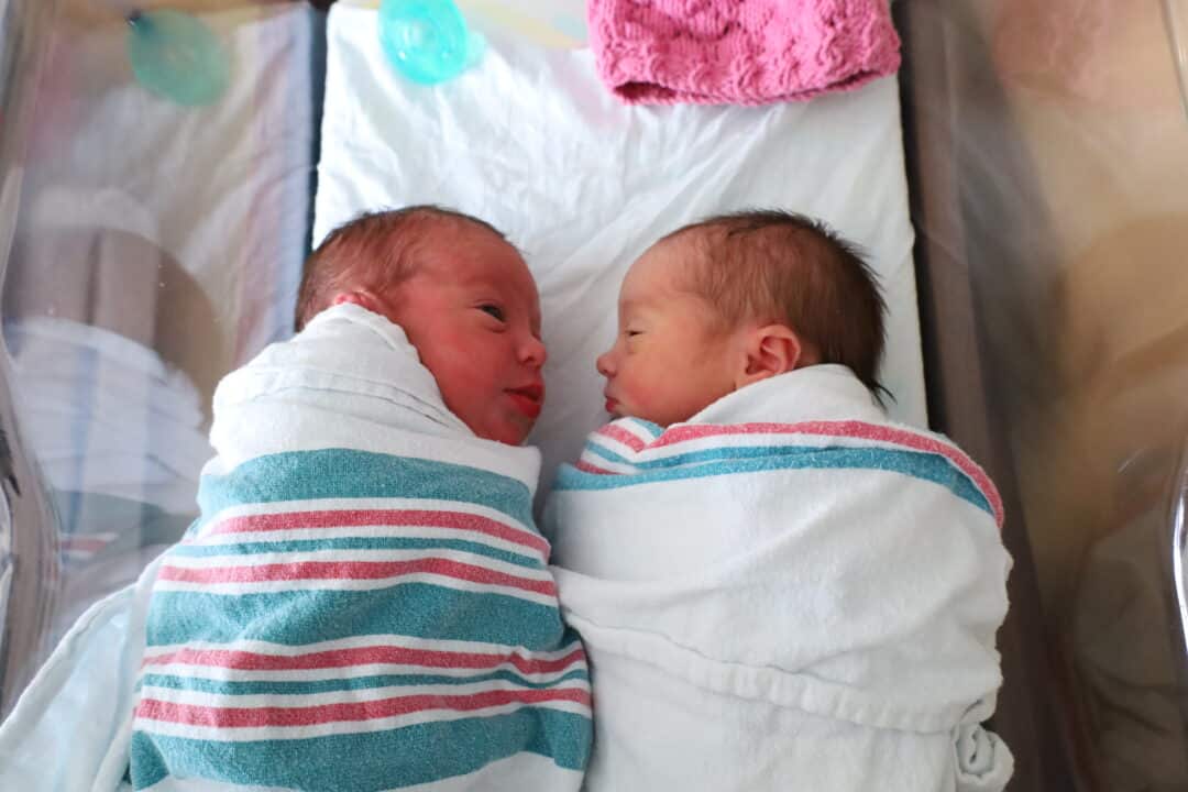 Swaddled twins face each other in a shared bassinet.