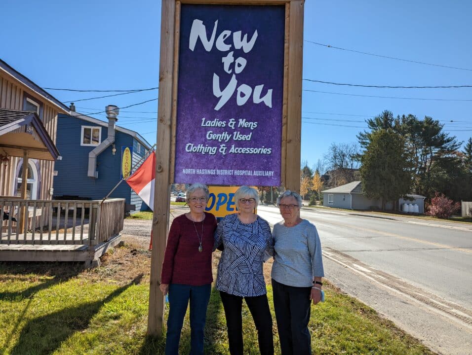Three volunteers standing in front of the “New to You” retail store sign outside.