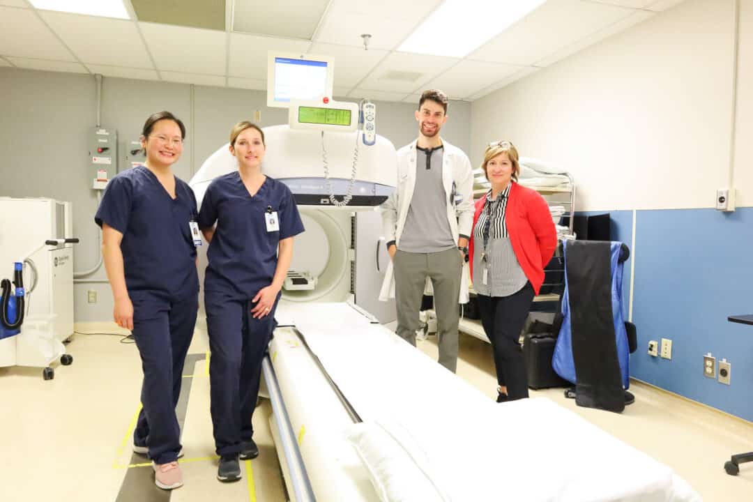 Nuclear Medicine technologists pose with a Gamma Camera.