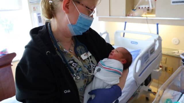 A nurse holds a swaddled newborn baby.
