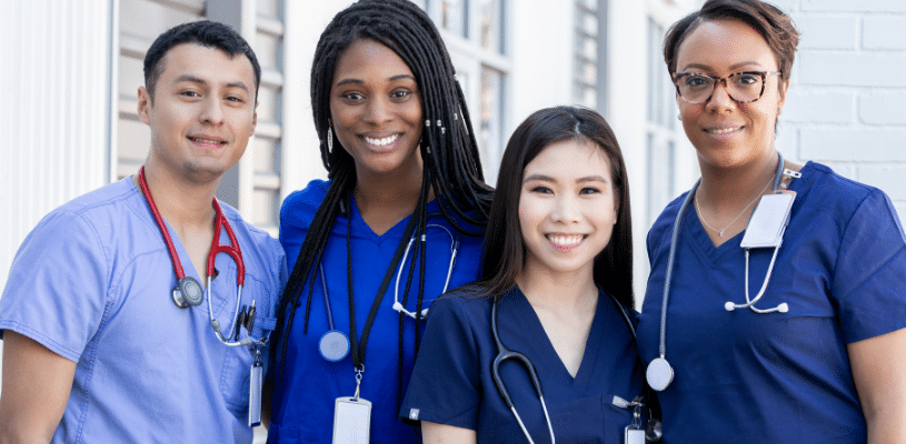Four, young multicultural students with stethoscopes around their necks stand together, smiling.
