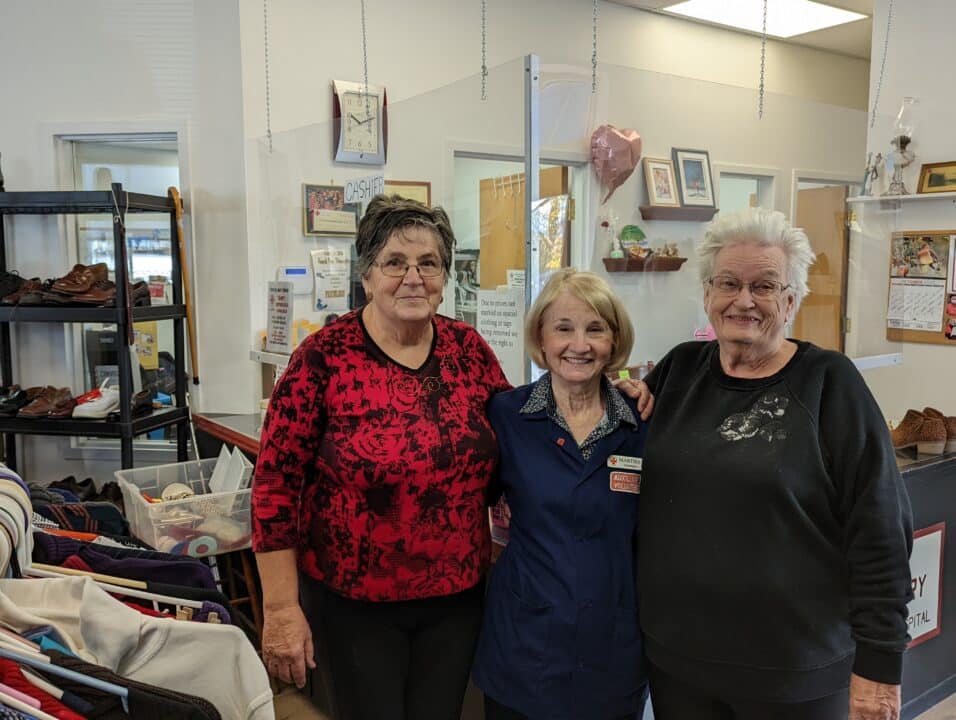 Female volunteers, Ana McCaw, Martha Finnegan, and Mabel Wilson, standing together in the Opportunity Shop.