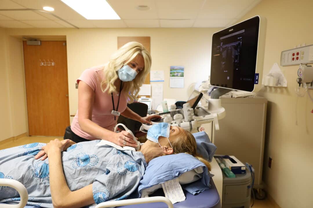 A sonographer uses an ultrasound machine on a patient’s neck.