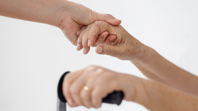 Two arms reaching out and holding hands with an another hand slightly out of focus holding a walking cane.