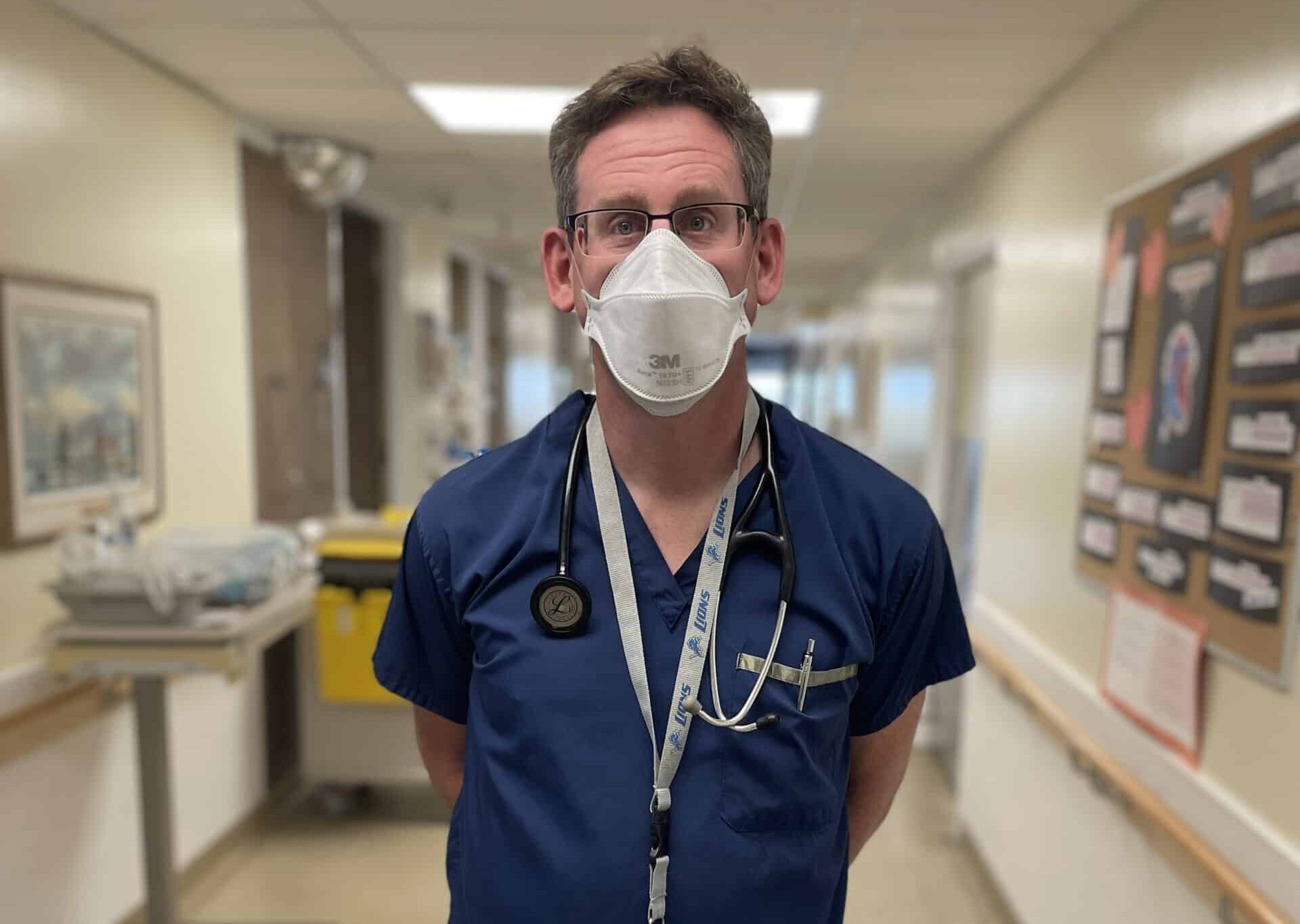 A doctor stands in a hallway wearing a mask.