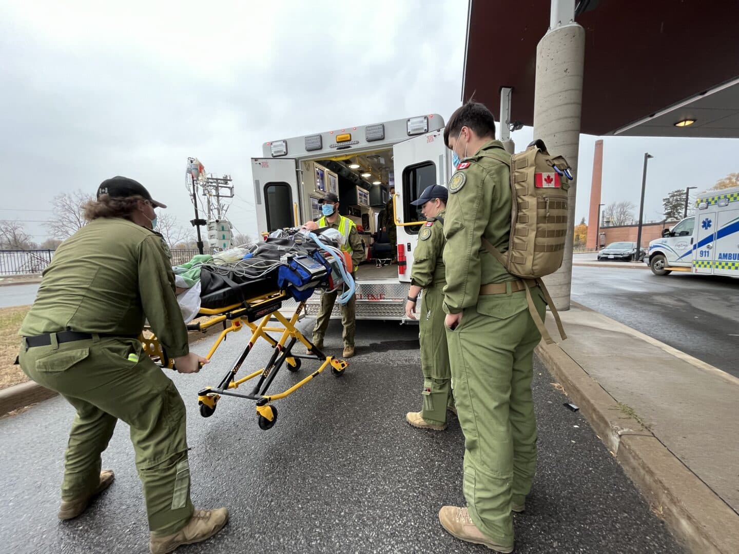 Military personnel load a simulated patient into an ambulance.