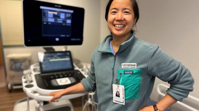 A smiling woman stands in front of an ultrasound machine.