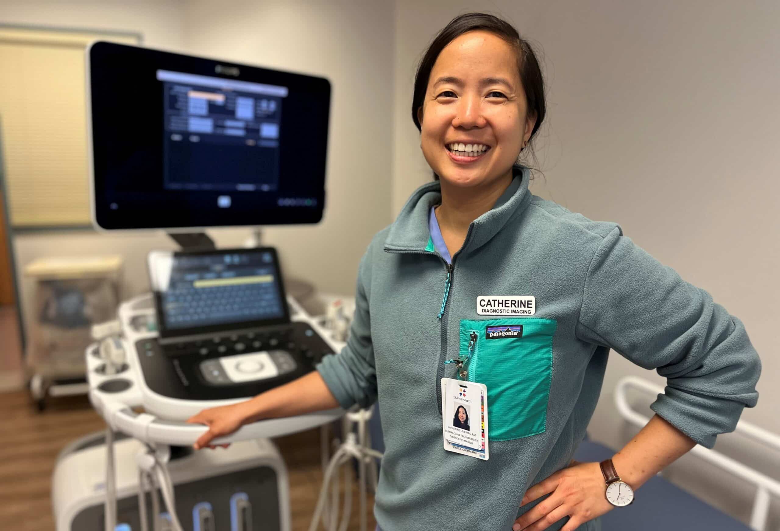 A smiling woman stands in front of an ultrasound machine.
