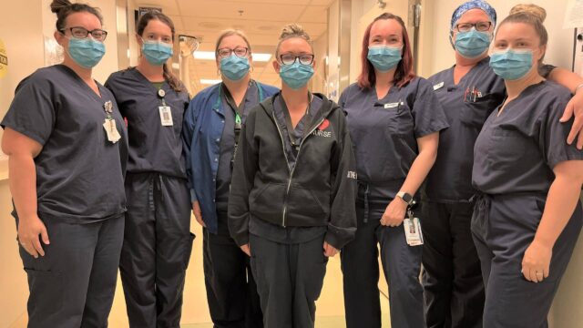 Seven nurses wearing scrubs and masks gather together for the photo.