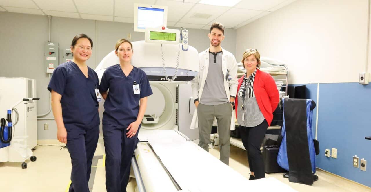 Four health care providers stand beside a Nuclear Medicine machine.