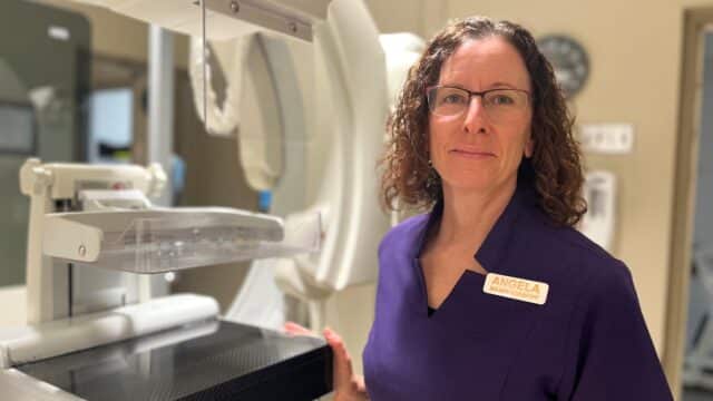 A Medical Radiation Technologists stands with her hand on a mammography machine