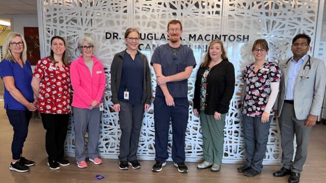 Eight hospital workers stand in front of a decorative cancer clinic wall.