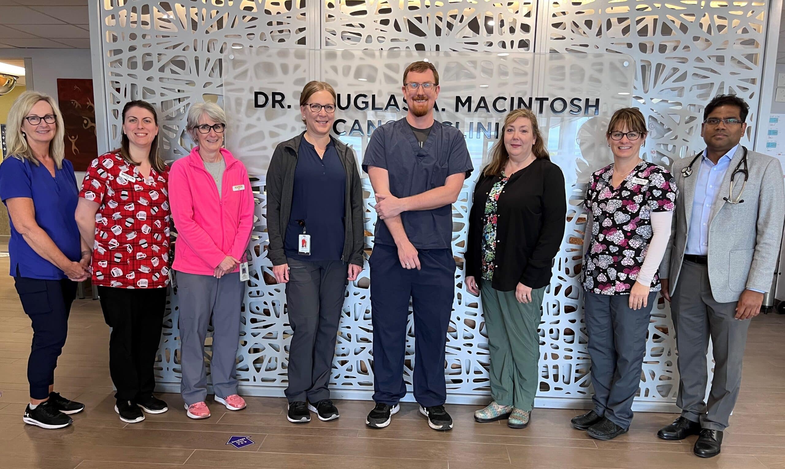 Eight hospital workers stand in front of a decorative cancer clinic wall.