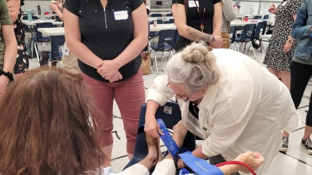 A healthcare provider wraps a velcro cuff around a participant's ankle while two other women watch.
