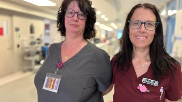Two women wearing hospital scrubs, glasses and name badges stand side-by-side.
