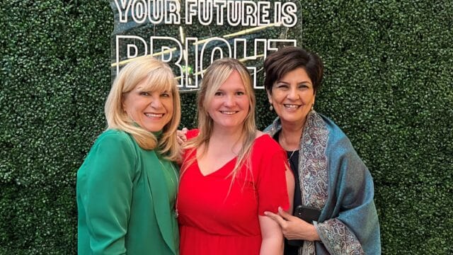 Three women stand smiling together in front of a green background and a sign that says Your Future is Bright.